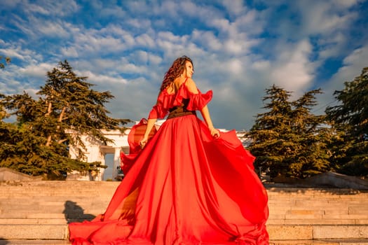 Sunrise red dress. A woman in a long red dress against the backdrop of sunrise, bright golden light of the sun's rays. The concept of femininity, harmony