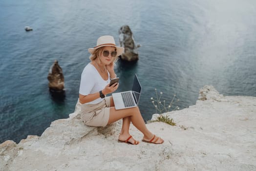 Freelance women sea working on the computer. Good looking middle aged woman typing on a laptop keyboard outdoors with a beautiful sea view. The concept of remote work