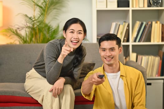 Happy young couple relaxing and watching TV together on a couch in cozy home. People and leisure activity concept.