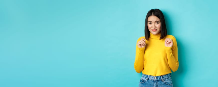 Image of disgusted chinese woman looking with cringe and aversion, grimacing and step backwards from something disgusting, standing over blue background.