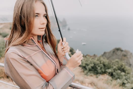 Woman rain park. Happy woman portrait wearing a raincoat with transparent umbrella outdoors on rainy day in park near sea. Girl on the nature on rainy overcast day