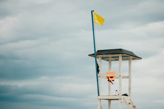 Empty white lifeguard tower with a yellow flag on the beach in windy weather. Beach lifeguard tower with yellow flag indicator. Nobody. Holiday recreation concept