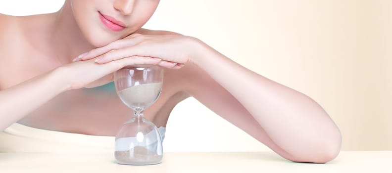 Closeup personable model holding hourglass in beauty concept of anti-aging skincare treatment. Young girl portrait with perfect smooth clean skin and flawless soft makeup in isolated background