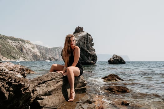 Woman travel sea. Young Happy woman in a long red dress posing on a beach near the sea on background of volcanic rocks, like in Iceland, sharing travel adventure journey