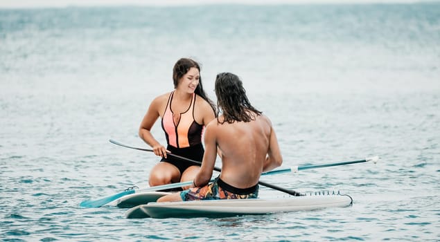 Sea woman and man on sup. Silhouette of happy young woman and man, surfing on SUP board, confident paddling through water surface. Idyllic sunset. Active lifestyle at sea or river