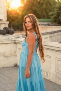 Woman sunset blue dress. Portrait of a woman with long hair and a blue dress against the backdrop of the setting sun and a white building. Lifestyle, walking around the city.