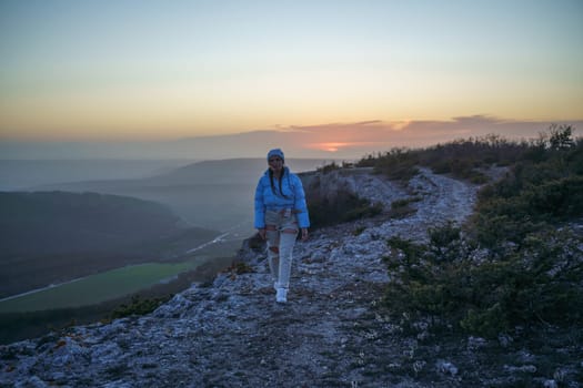 Woman tourist on top of sunrise mountain. The girl salutes the sun, wearing a blue jacket, white hat and white jeans. Conceptual design