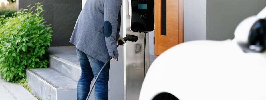 Closeup progressive asian man install cable plug to his electric car with home charging station. Concept of the use of electric vehicles in a progressive lifestyle contributes to clean environment.