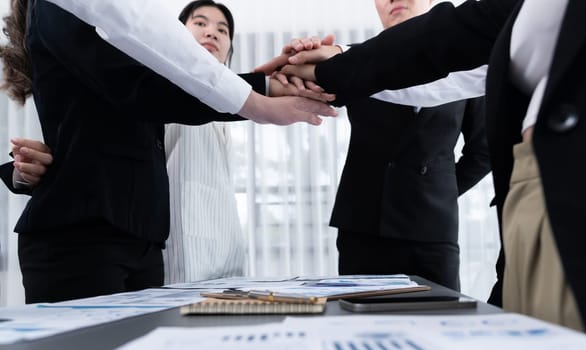 Closeup business team of suit-clad businessmen and women join hand stack together and form circle. Colleague collaborate and work together to promote harmony and teamwork concept in office workplace.