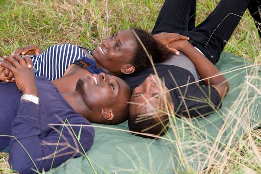 Happy group of young friends lying on the grass outdoors and looking overhead in the sky