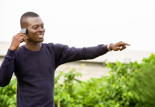 young man standing outdoors communicates and shows something of the finger while smiling.