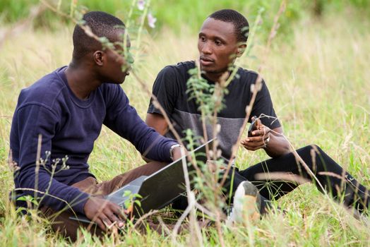two young students talk, work in front of a laptop and relax while sitting in the park.