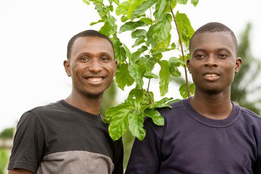 young people standing outdoors near a plant smiling on camera.