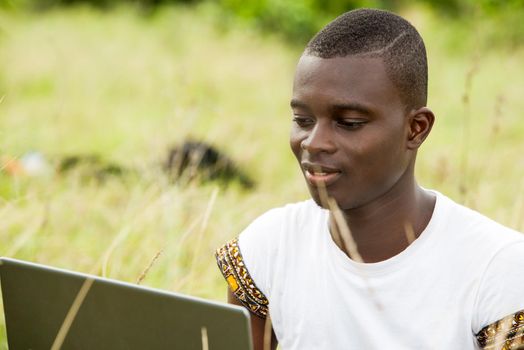 young man sitting in the grass with laptop computer browsing smiling.