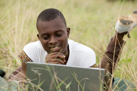 young man lying in grass watching computer smiling.