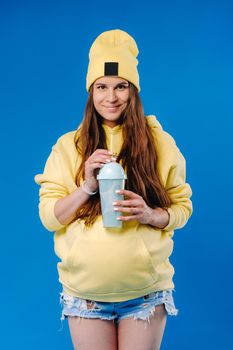 pregnant girl in yellow clothes with a glass of juice on a blue background.