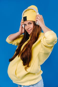 A pregnant girl in a yellow jacket and headphones stands on a blue background.