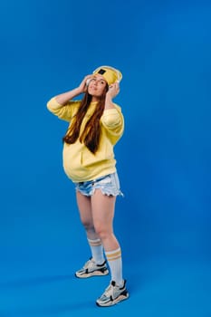 A pregnant girl in a yellow jacket and headphones stands on a blue background.