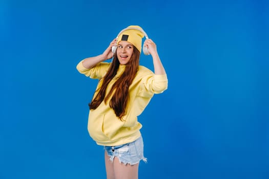 A pregnant girl in a yellow jacket and headphones stands on a blue background.