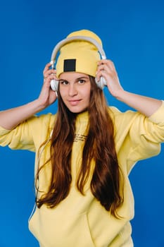 A pregnant girl in a yellow jacket and headphones stands on a blue background.