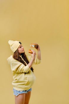 pregnant girl in yellow clothes with hamburgers in her hands on a yellow background.