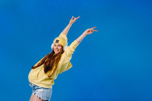 A pregnant girl in a yellow jacket and headphones stands on a blue background.