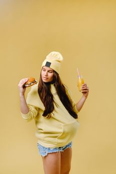 pregnant girl in yellow clothes with hamburgers in her hands on a yellow background.