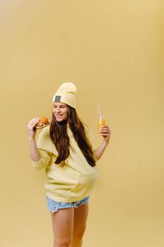 pregnant girl in yellow clothes with hamburgers in her hands on a yellow background.