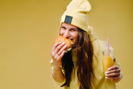 pregnant girl in yellow clothes with hamburgers in her hands on a yellow background.