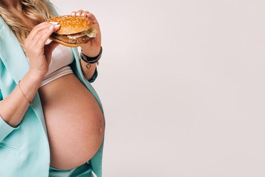 Close-up of a pregnant girl in a suit with hamburgers in her hands on a gray background.
