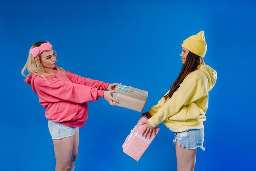 Two pregnant girls with gifts in their hands on a blue isolated background.