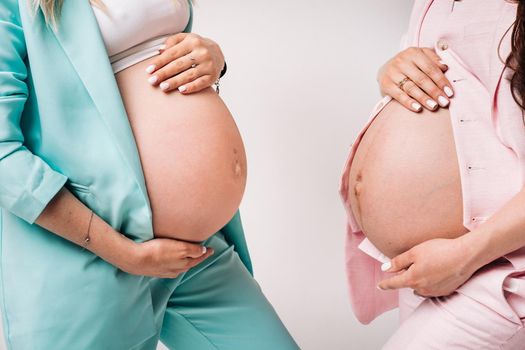 Two pregnant women in suits close-up on a gray background.
