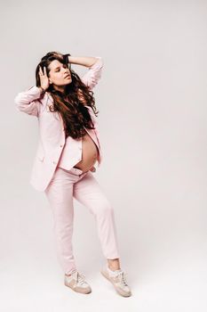 pregnant woman in pink suit close-up on gray background.