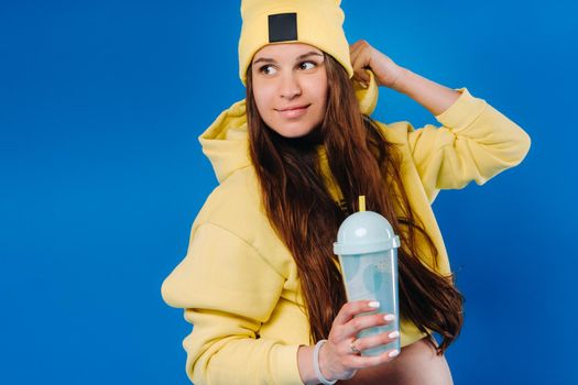 pregnant girl in yellow clothes with a glass of juice on a blue background.