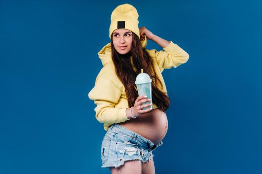 pregnant girl in yellow clothes with a glass of juice on a blue background.