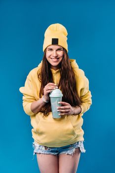 pregnant girl in yellow clothes with a glass of juice on a blue background.
