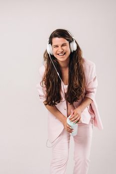 a pregnant woman in a pink suit with headphones emotionally listens to music on a gray background.
