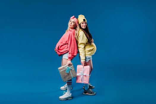 Two pregnant girls with gifts in their hands on a blue isolated background.