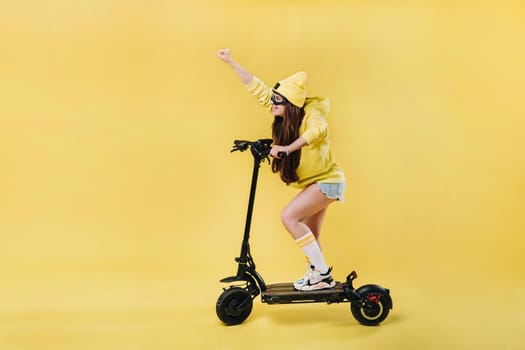 A pregnant girl in yellow clothes on an electric scooter on an isolated yellow background.