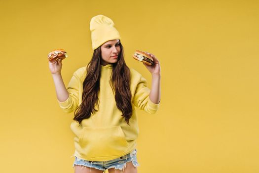 pregnant girl in yellow clothes with hamburgers in her hands on a yellow background.
