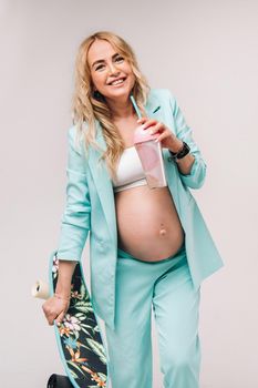 pregnant girl in turquoise clothes with a glass of juice and a skateboard in her hands on a blue background.