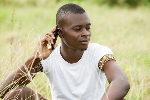 Portrait of a young man sitting in the grass uses and communicates with the mobile phone outdoors