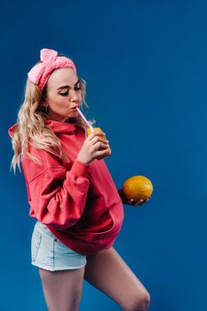 pregnant girl in pink clothes with a bottle of juice and a melon on a blue background.