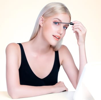 Personable woman with blond hair putting black mascara with brush in hand on long thick eyelash. Perfect fashionable cosmetic clean facial skin with beautiful eye young woman in high resolution.