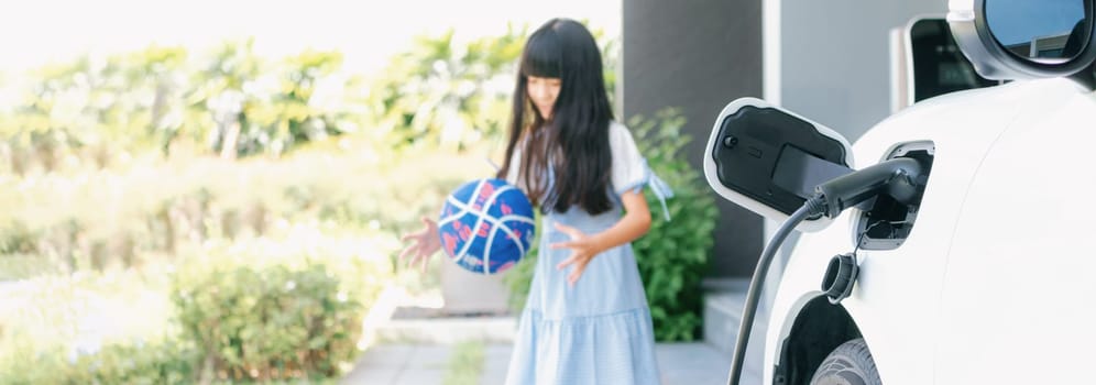 Focus home electric charging station for electric vehicle as alternative clean sustainable energy technology concept with blurred progressive young girl playing in the background at her home.