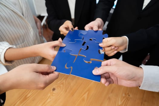 Closeup top view business team of office worker putting jigsaw puzzle together over table filled with financial report paper in workplace with manager to promote harmony concept in meeting room.
