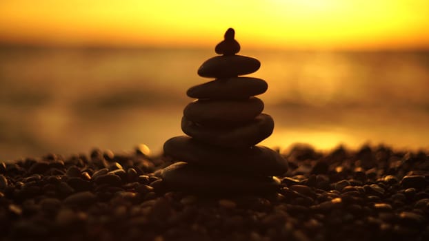 Balanced rock pyramid on pebbles beach. Golden sea bokeh on background. Selective focus, zen stones on sea beach, meditation, spa, harmony, calm, balance concept