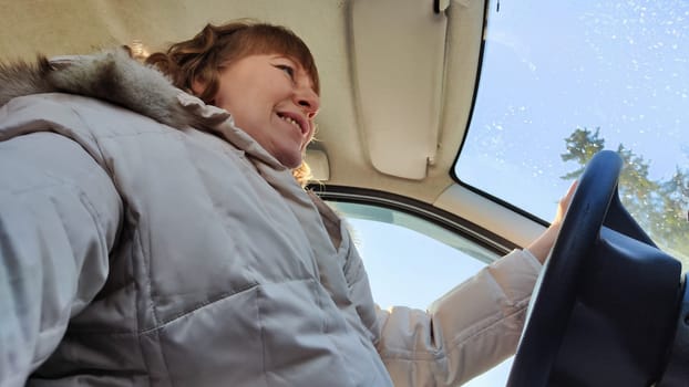 Woman sitting in the car in road trip. Blonde senior Woman driving transport. Lady travelling in cold time