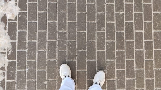 Abstract gray stone and brick urban tiles background and texture and legs in white jeans and sneakers