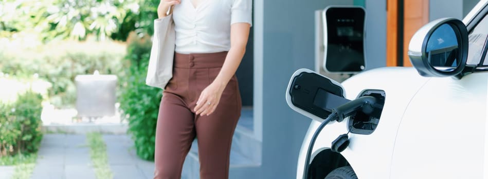 Progressive asian woman and electric car with home charging station. Concept of the use of electric vehicles in a progressive lifestyle contributes to a clean and healthy environment.